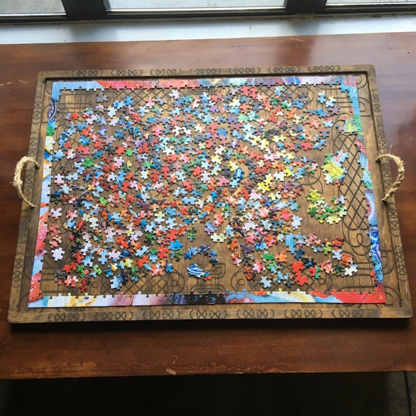 Jigsaw puzzle in progress on a wooden tray with rope handles
