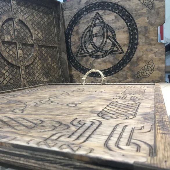 Wooden board and engraved lid with a triquetra knot, standing in the workshop