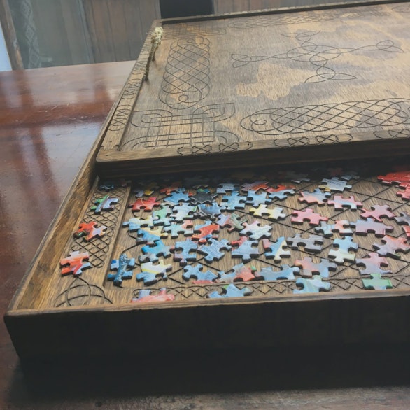 Wooden sorting tray with a knotwork-engraved lid, containing jigsaw puzzle pieces